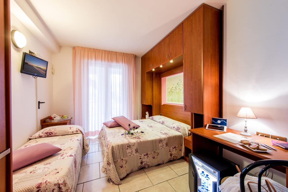 Habitación de hotel con dos camas, un escritorio, televisión y refrigerador.