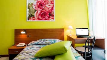 Una habitación de hotel con una cama, un escritorio con una computadora portátil, un teléfono y un cuadro de rosas en la pared.