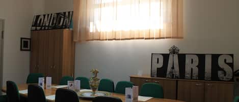 A conference room with a wooden table, green chairs, a large 'LONDON' sign, a 'PARIS' sign, and a vase with flowers.