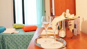 Une chambre d’hôtel avec un lit, un plateau avec des verres et une bouteille, et une fenêtre avec des rideaux.