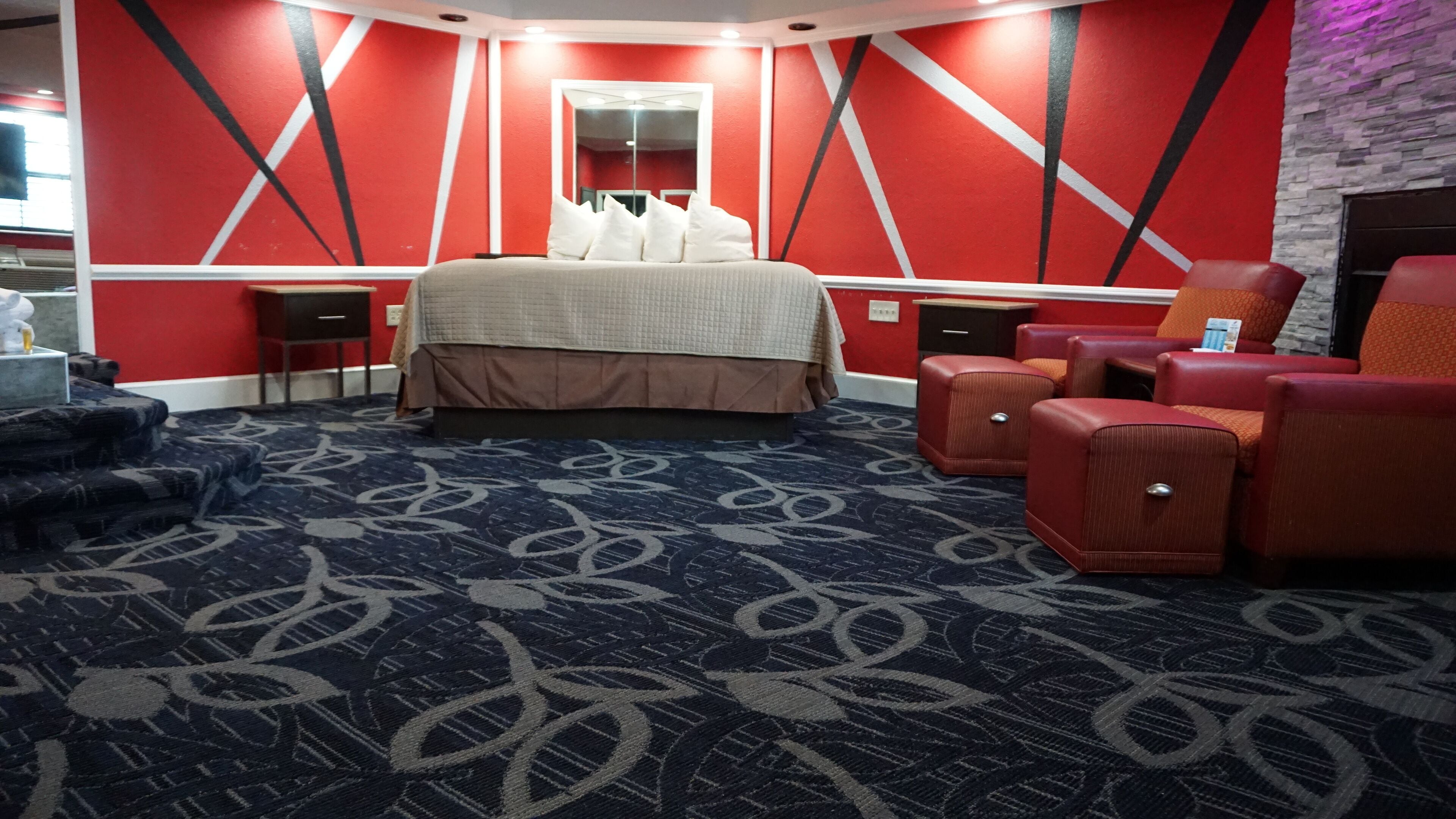 A hotel room with a large bed, red walls, a mirror, a red sofa, and a patterned carpet.