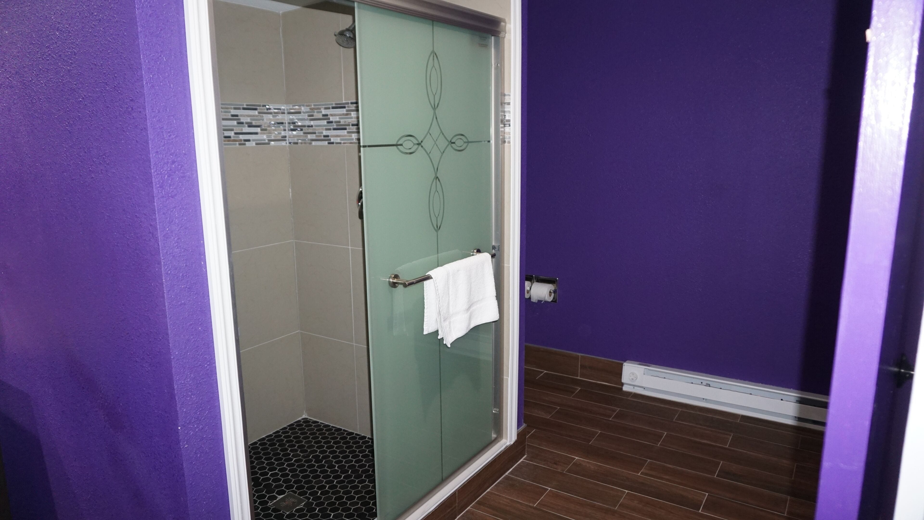 A bathroom with a glass shower door, a white towel hanging on the door handle, and a tiled floor.