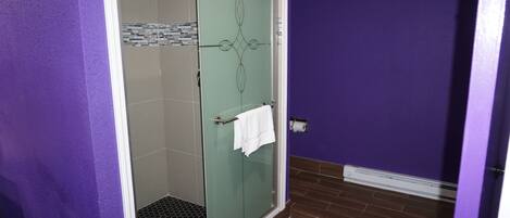 A bathroom with a glass shower door, a white towel hanging on the door handle, and a tiled floor.