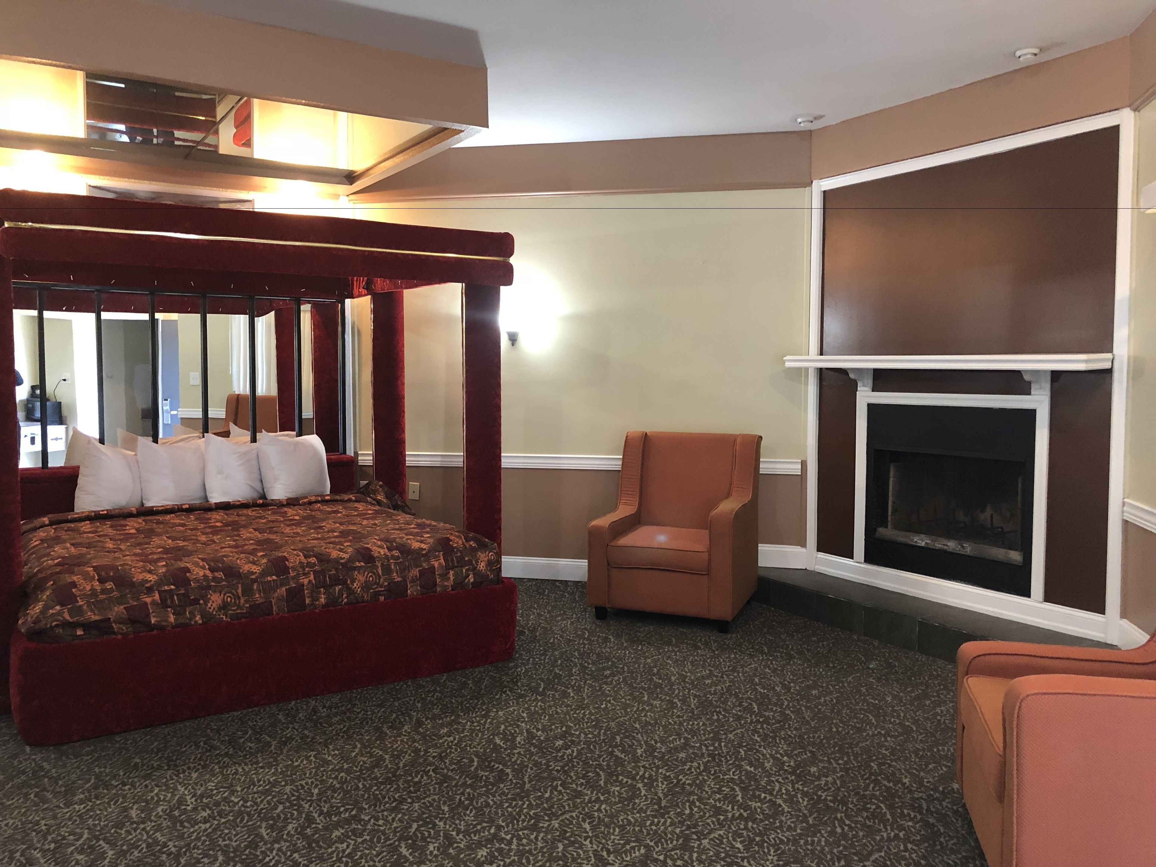 A hotel room with a four-poster bed, a fireplace, and a chair.