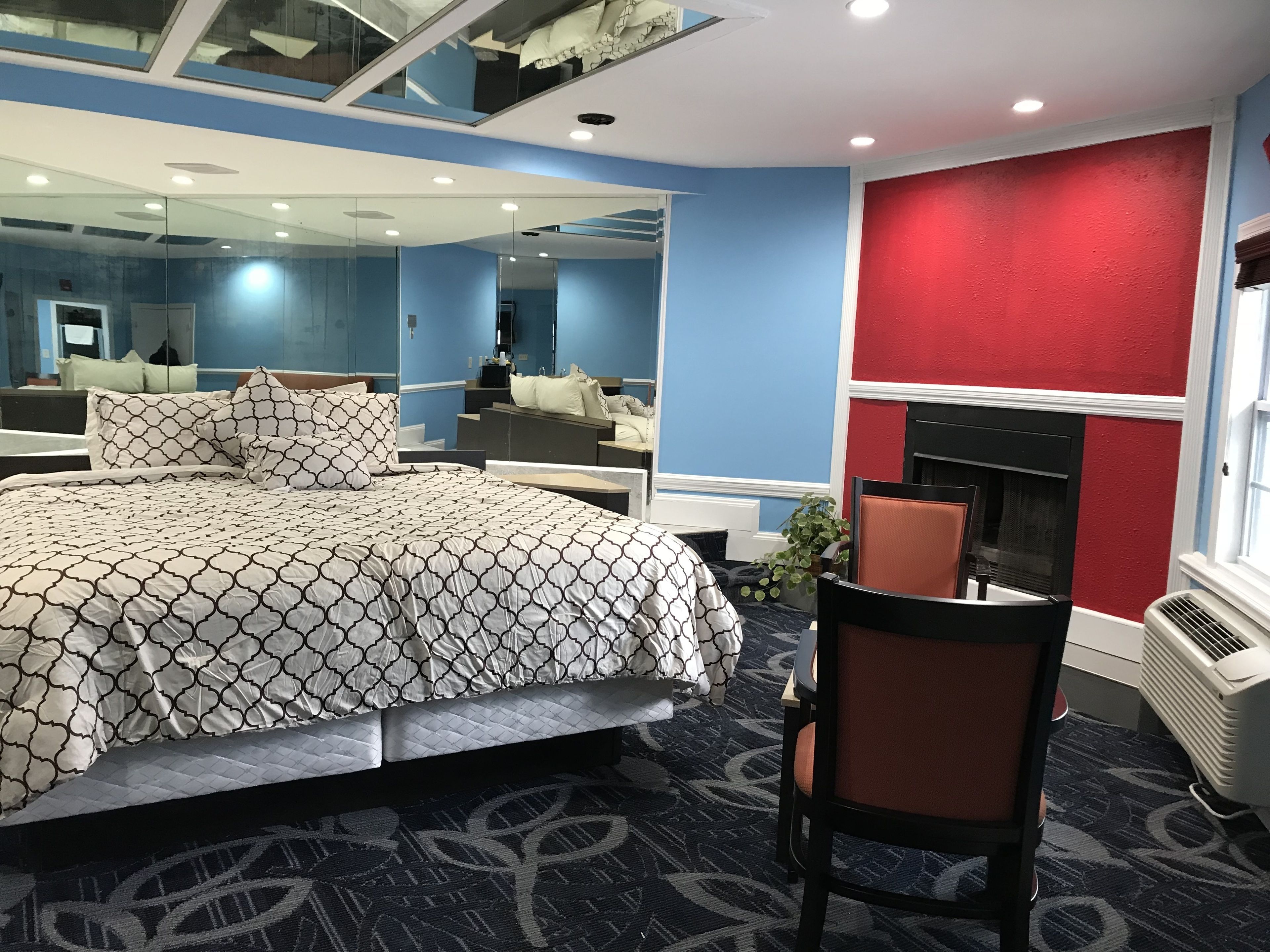 Una habitación de hotel moderna con una cama grande, un espejo, una pared de acento roja y una chimenea.