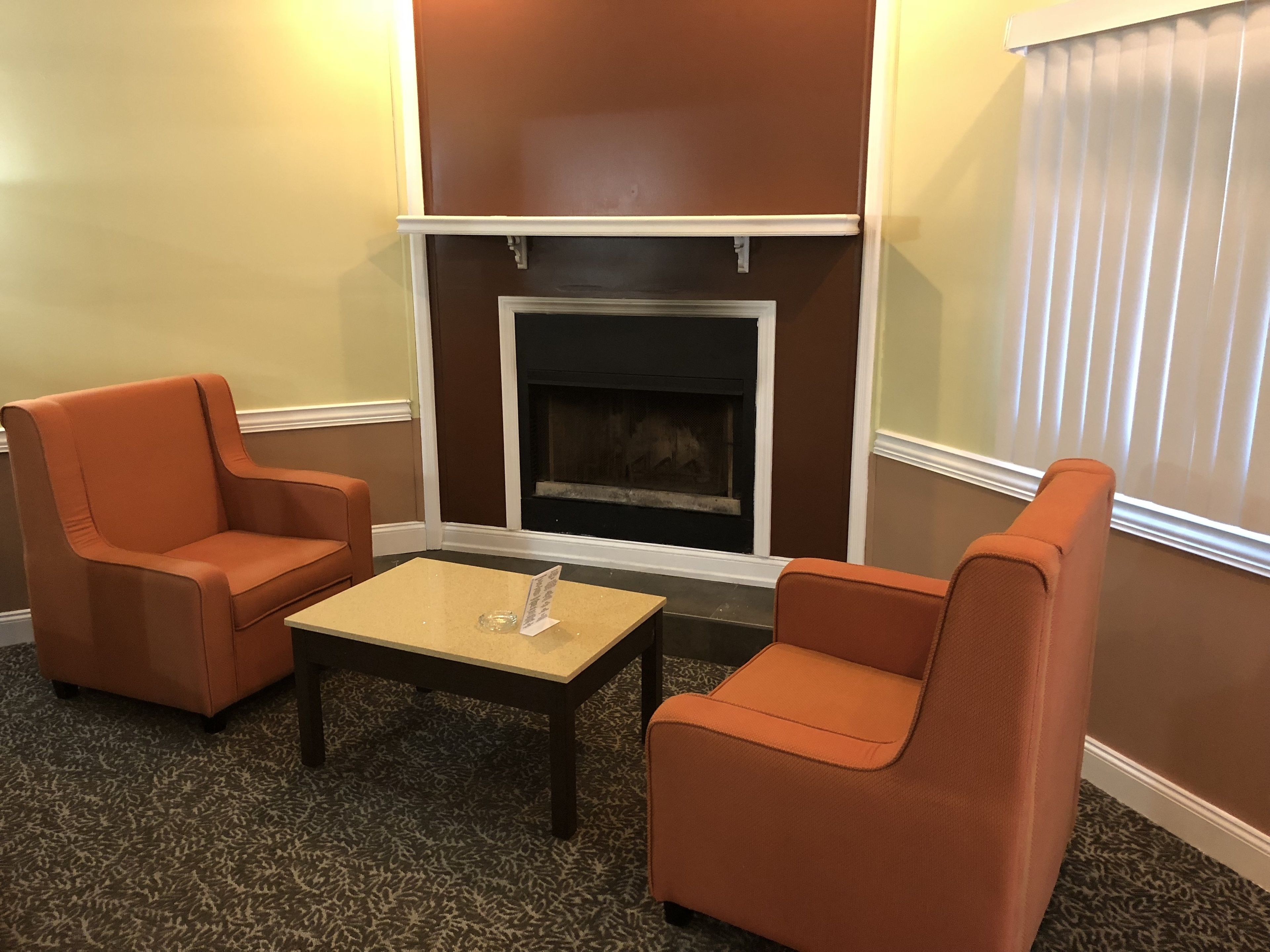A room with two orange armchairs, a small table, and a fireplace.