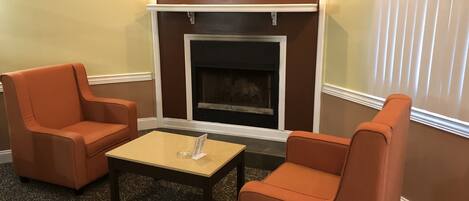 A room with two orange armchairs, a small table, and a fireplace.