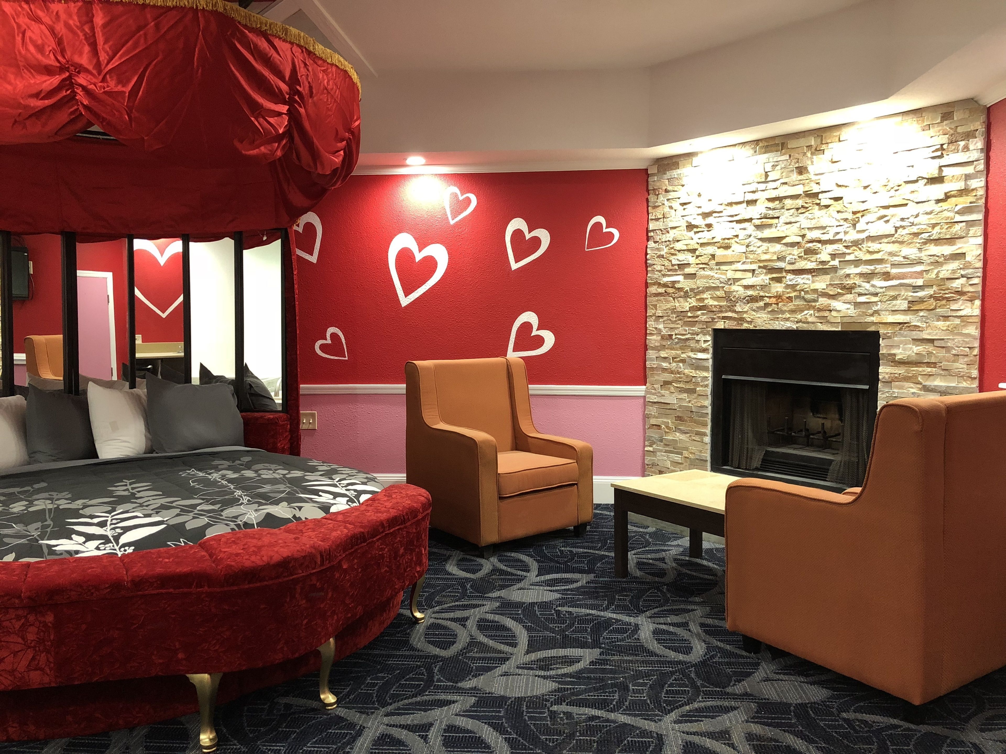 A cozy room with a red bed, a fireplace, and heart-shaped wall decorations.