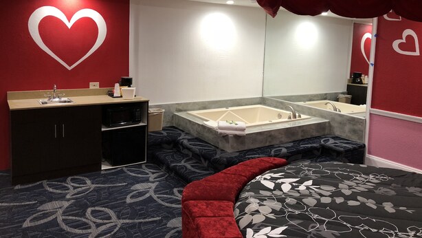 A modern bathroom with a vanity, a large mirror, a bathtub, and a red heart-themed wall.