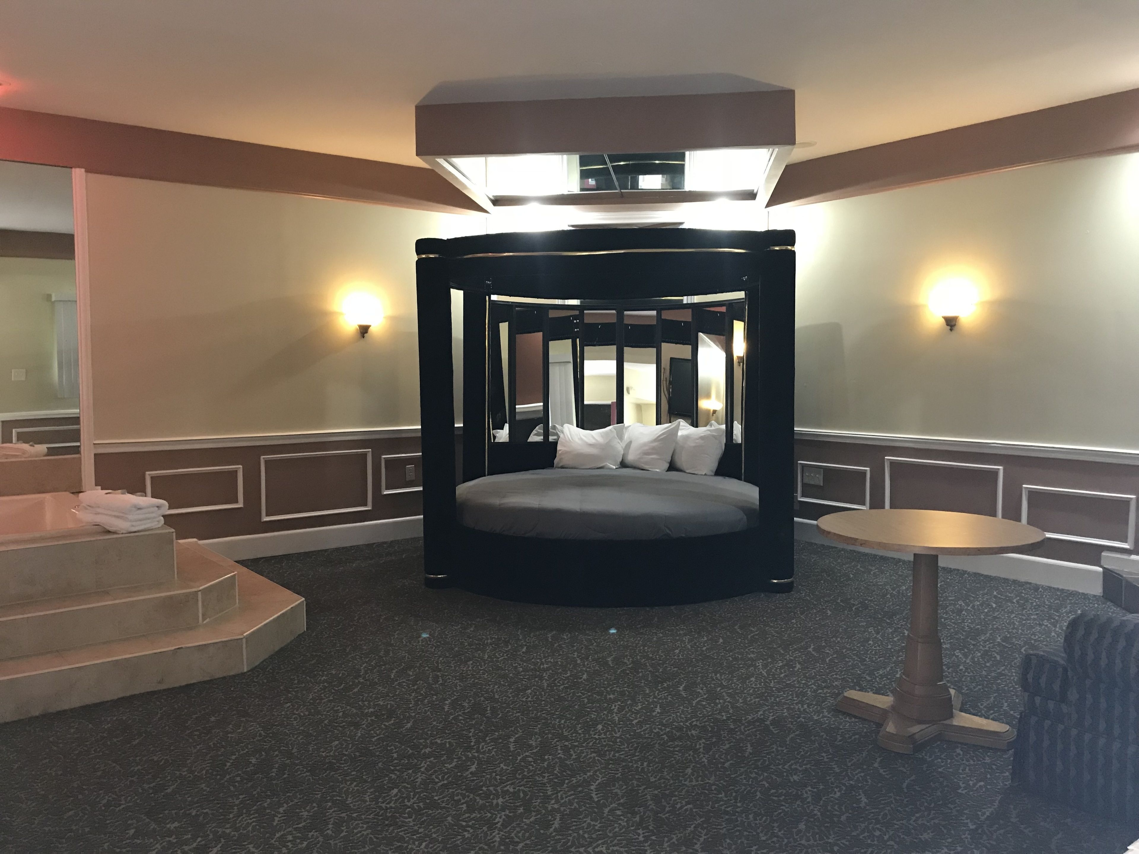 A circular bed with a canopy in a hotel room, a small round table, and a staircase.
