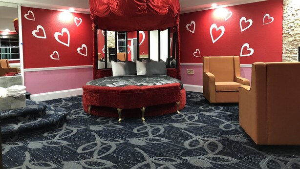 A room with a canopy bed, red walls with heart designs, a stone accent wall, and a patterned carpet. - Inn of the Dove (Cherry Hill)