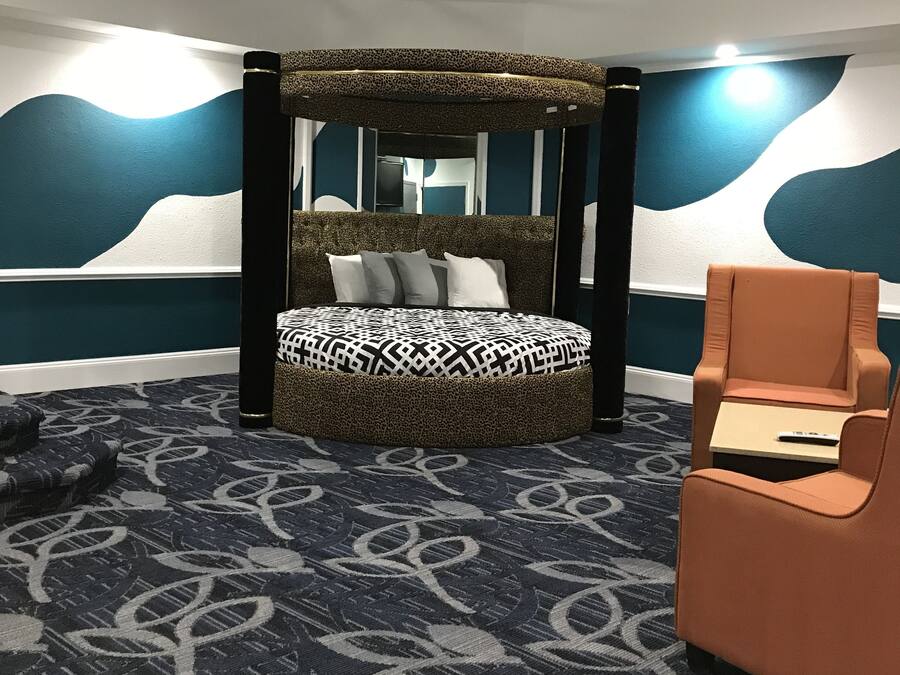 Ein Schlafzimmer mit Himmelbett, rundem Ottomanen, einem Sessel und einem gemusterten Teppich.