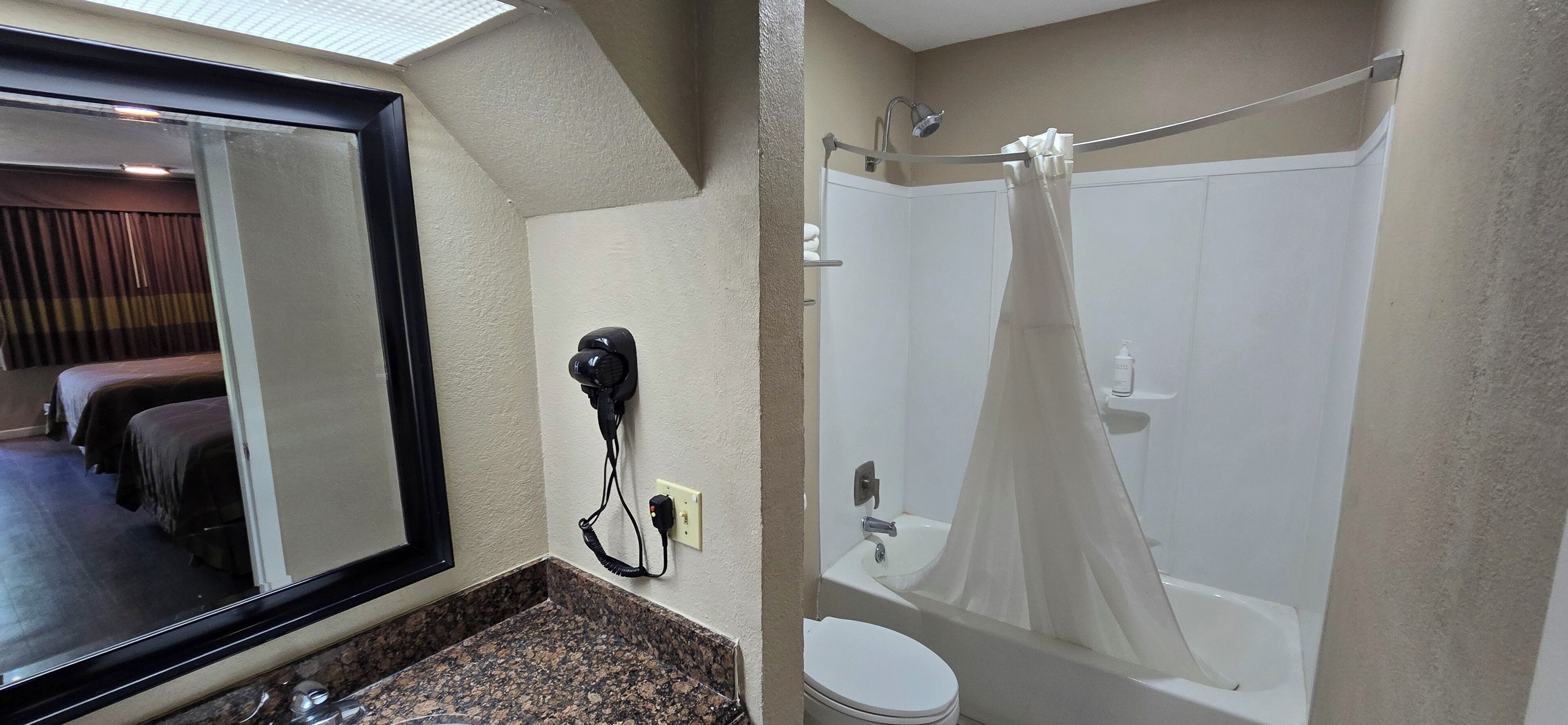 Une salle de bain d’hôtel équipée d’une douche, de toilettes et d’un sèche-cheveux fixé au mur.