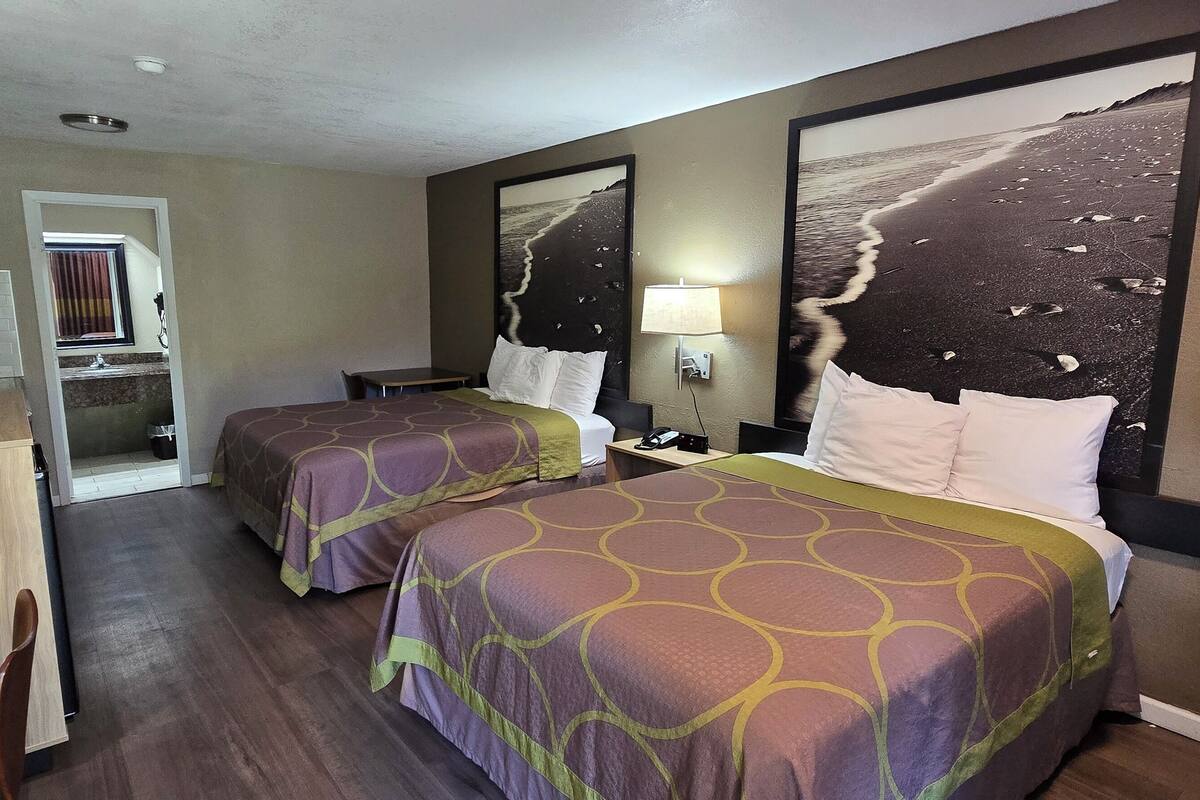 Ett hotellrum med två sängar, ett skrivbord, en tv och ett badrum som syns genom en öppen dörr.