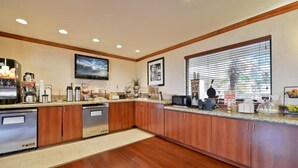 A modern kitchen with stainless steel appliances, wooden cabinets, and a large window with blinds.