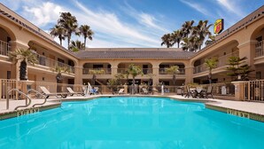 A pool area with lounge chairs and palm trees, surrounded by a multi-level building with balconies.