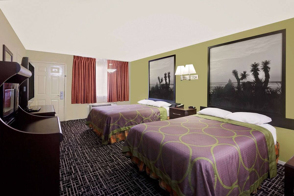 Ett hotellrum med två sängar, ett skrivbord med en dator, en TV och ett stort fönster med gardiner.