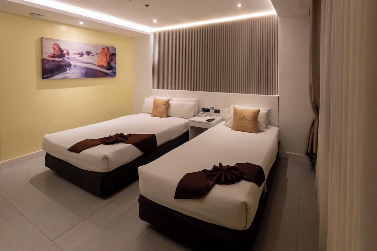 Habitación de hotel con dos camas, un cuadro en la pared, una mesita de noche con un teléfono y una ventana con cortinas.