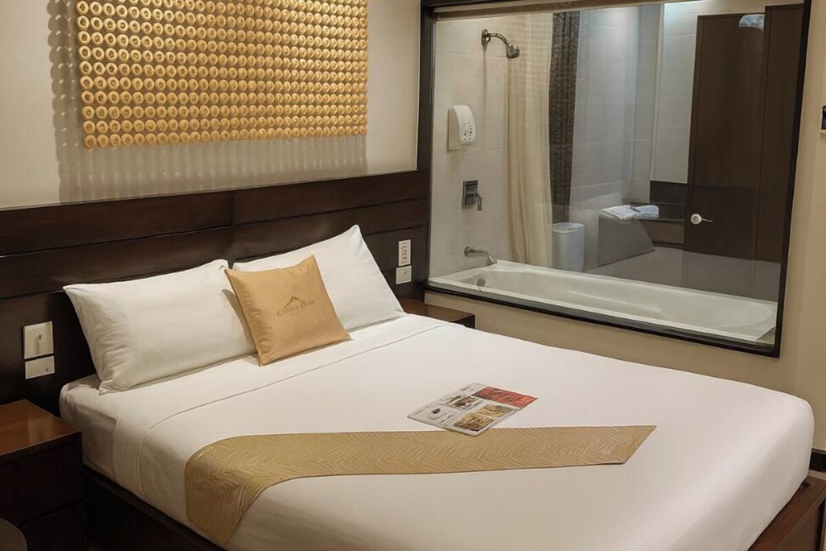 A DELUXE Queen Bed in a Castle Peak Hotel room with a large mirror, a shower, and a textured wall panel.