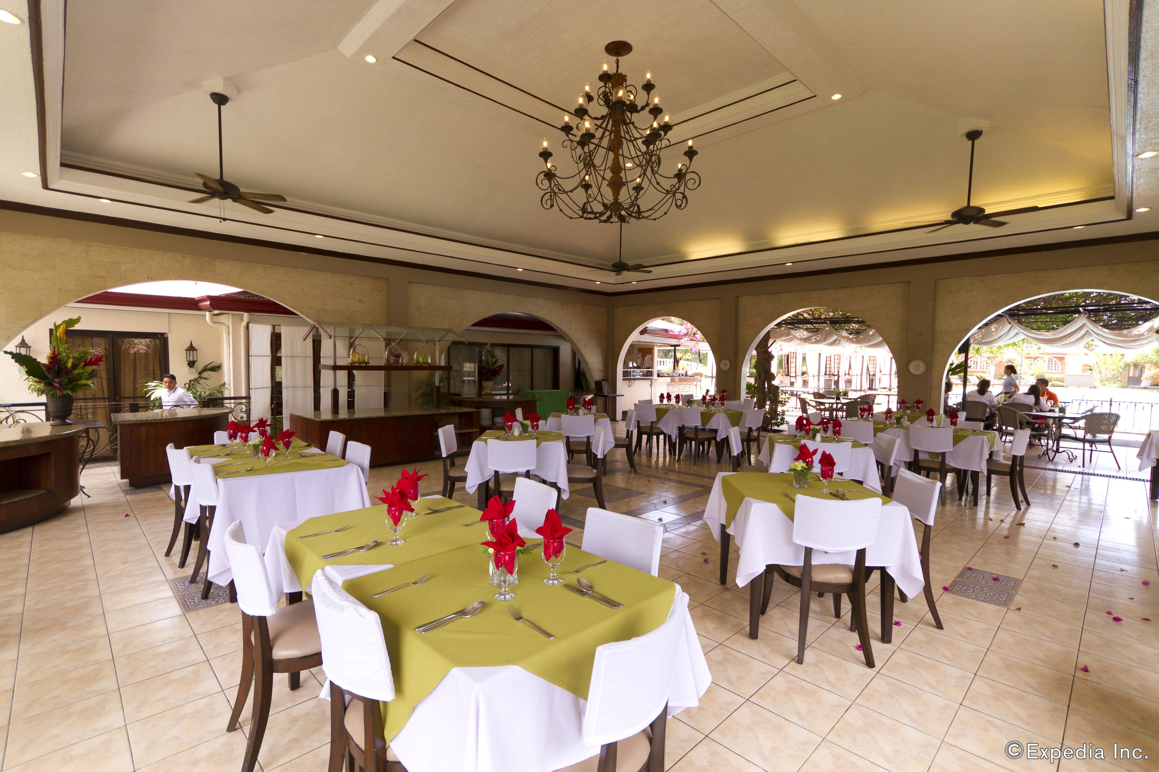 A spacious dining area with multiple tables set for dining, featuring white tablecloths and green centerpieces.