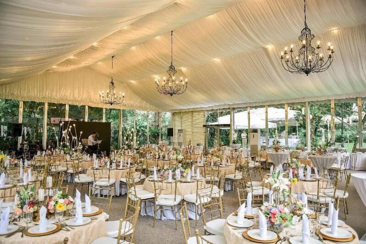 Een evenementenruimte met tenten, ronde tafels, gouden stoelen en kroonluchters.