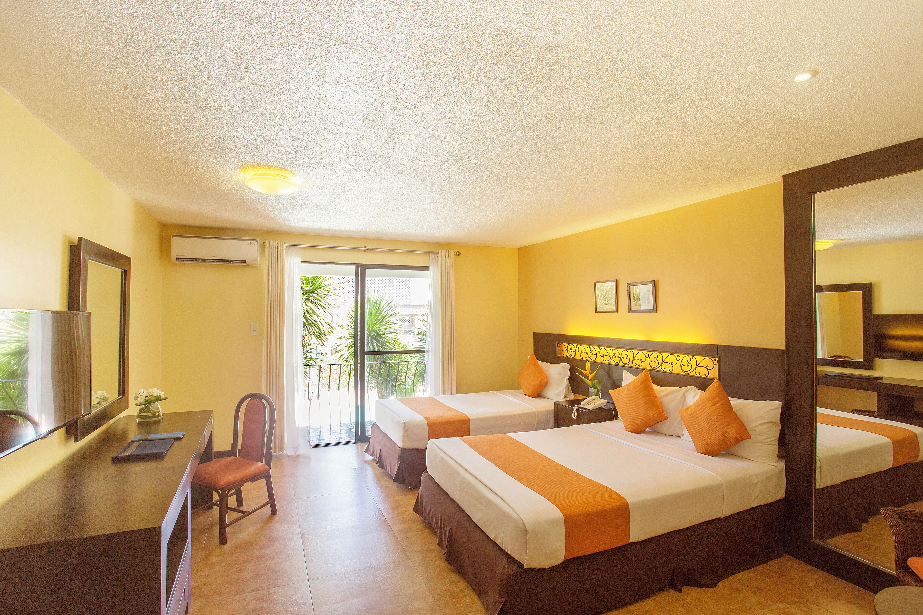 Habitación de hotel con dos camas, un escritorio, una silla y un espejo grande.