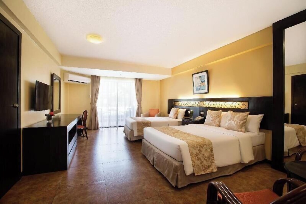 Quarto de hotel com duas camas, uma escrivaninha, uma cadeira, uma televisão e uma janela grande com cortinas.