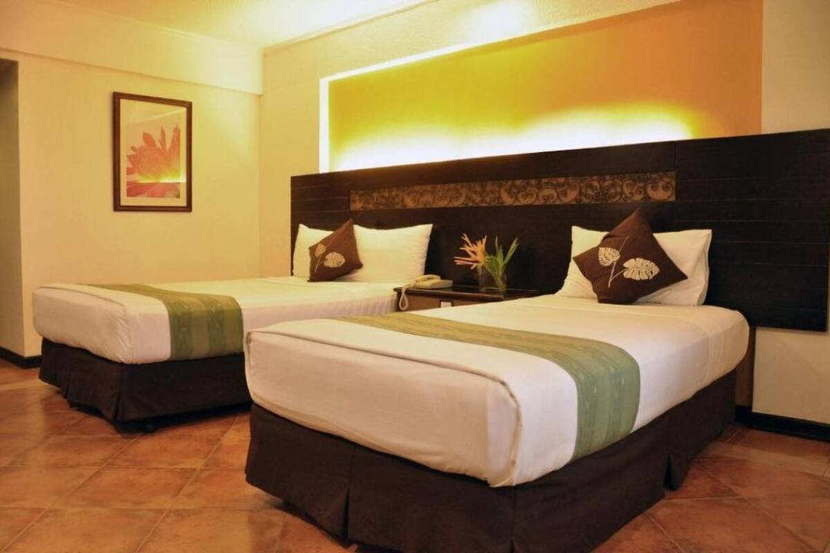 Een hotelkamer met twee bedden, elk met hoofdeinde, nachtkastje en een ingelijst schilderij aan de muur.