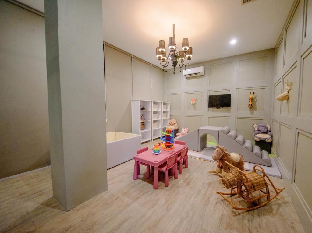 Un salón infantil con una mesa rosa, sillas y juguetes. Hay una estantería, un corralito y un caballo balancín.