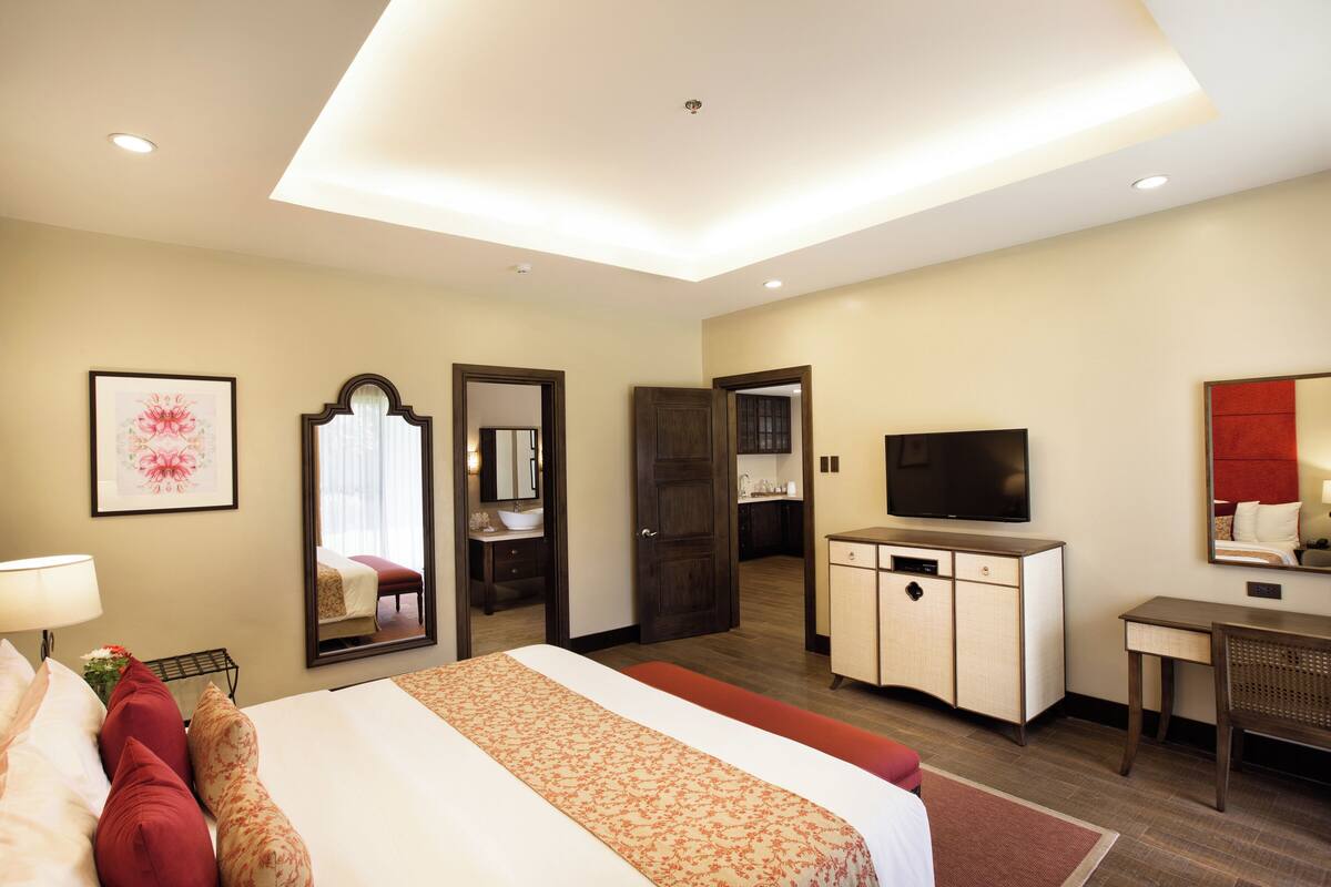 Hotelkamer met een groot bed, een bureau, een televisie, een spiegel en een badkamer door een geopende deur.