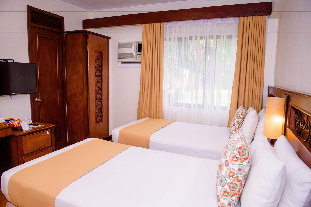 Een hotelkamer met twee bedden, een televisie, een kast en een raam met gordijnen.