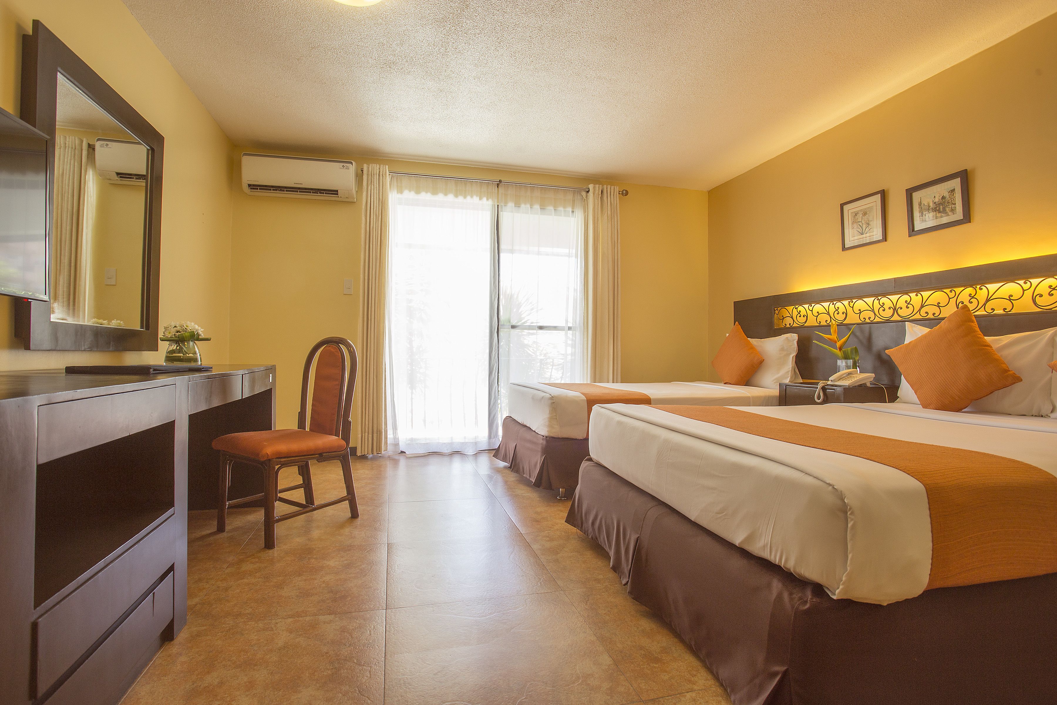 Ein Hotelzimmer mit zwei Betten, einem Schreibtisch, einem Stuhl und einem großen Spiegel.