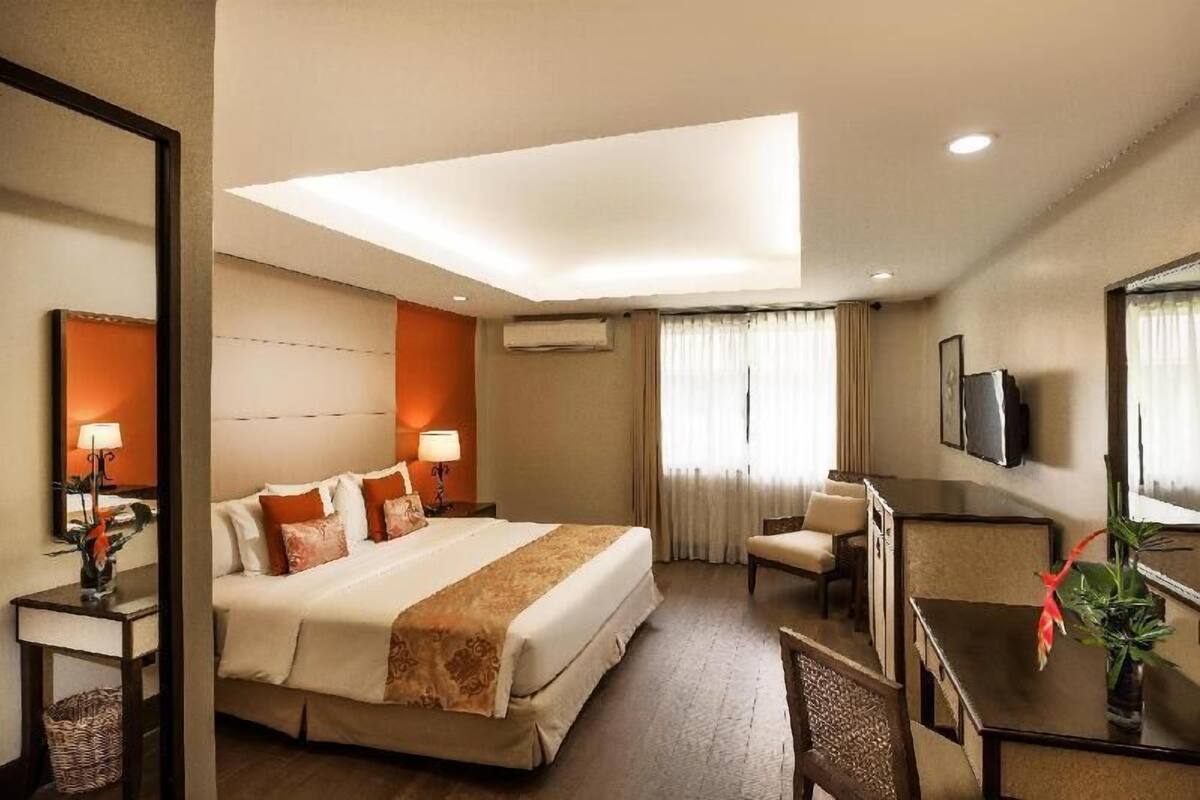 Een hotelkamer met een groot bed, nachtkastjes, een bureau, een stoel, een televisie en een raam met gordijnen.