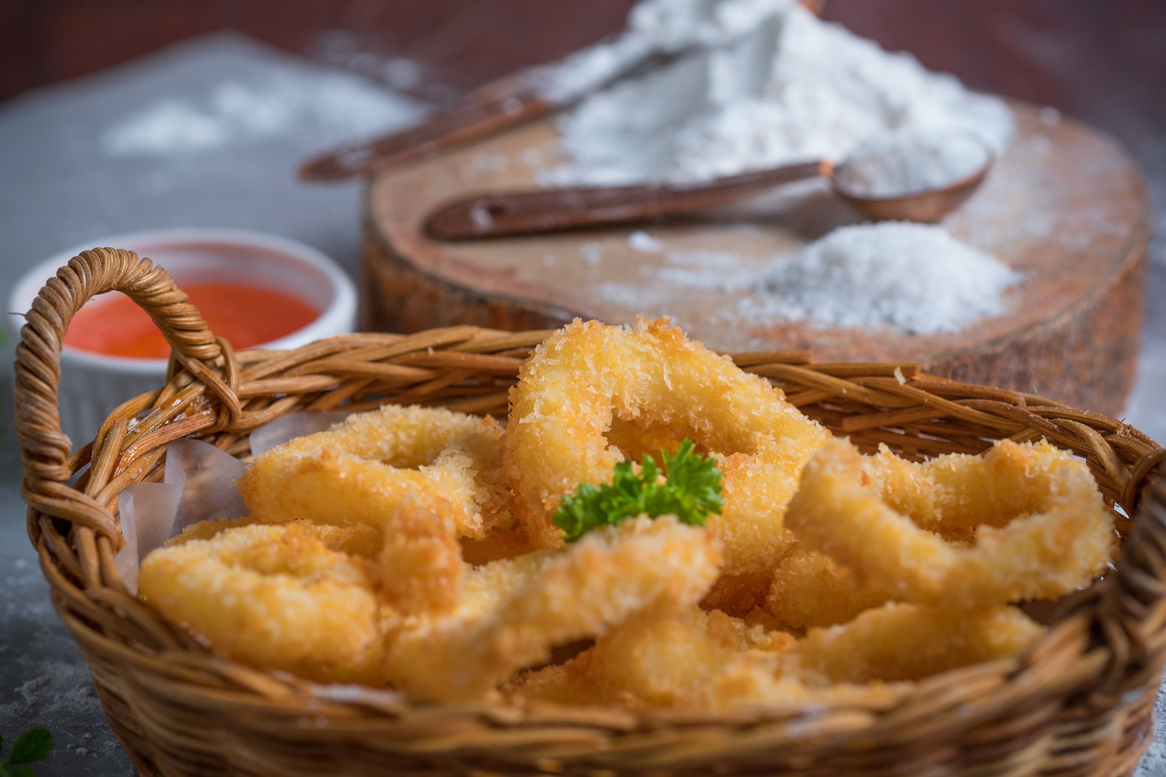 Una cesta de comida frita con salsa para mojar y una tabla de madera con harina.