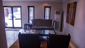 A living room with a sofa, two armchairs, a coffee table, and a TV. There is a door leading outside, and an air conditioning unit is mounted on the wall. - S&S Hotels and Suites (Lagos)