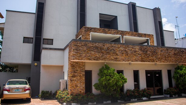 A modern building with a stone facade, a car parked in front, and a clear sky. - S&S Hotels and Suites (Lagos)