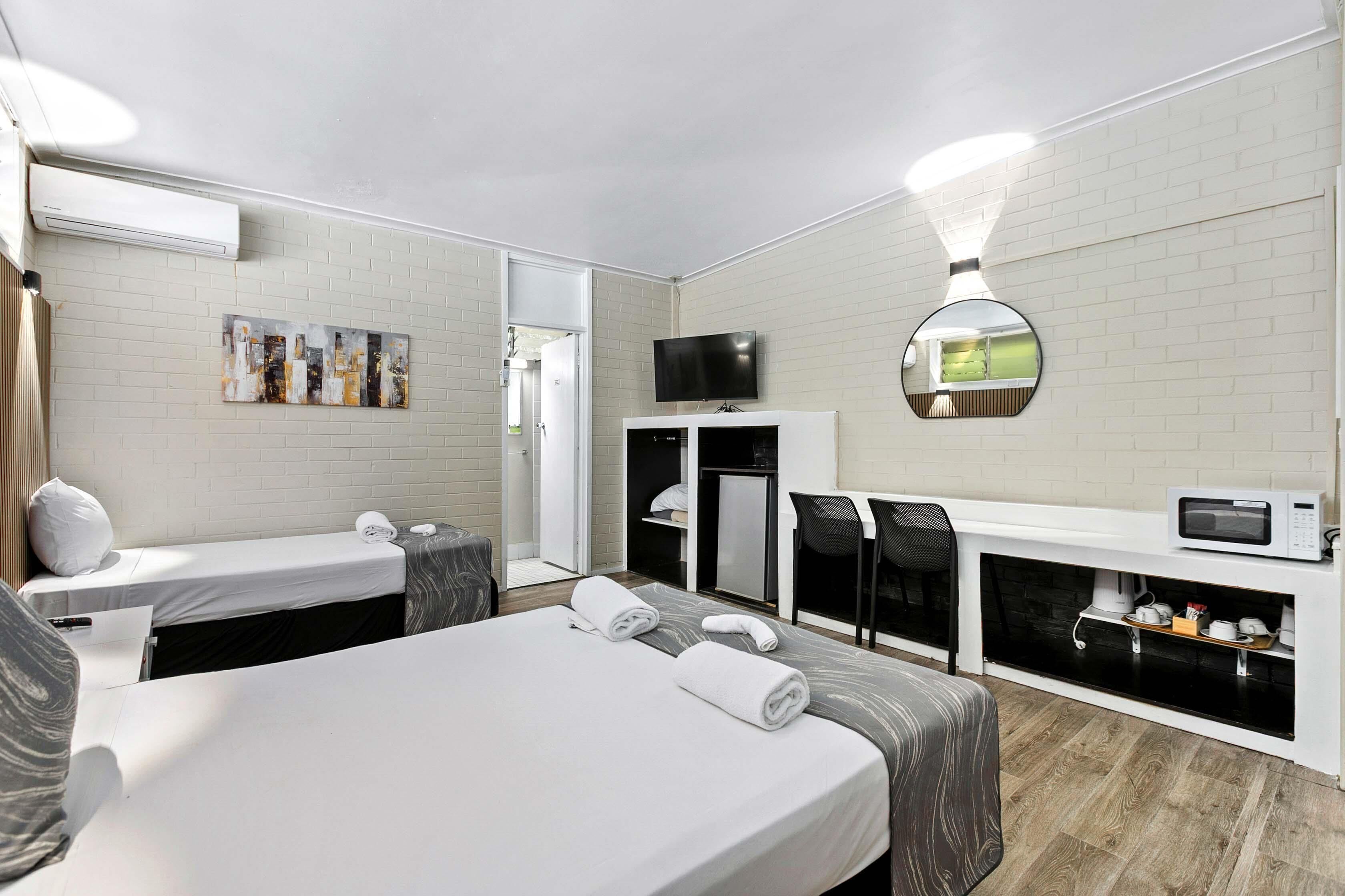 Une chambre d’hôtel avec un grand lit, un bureau avec une chaise, une télévision, un four à micro-ondes et une petite kitchenette.