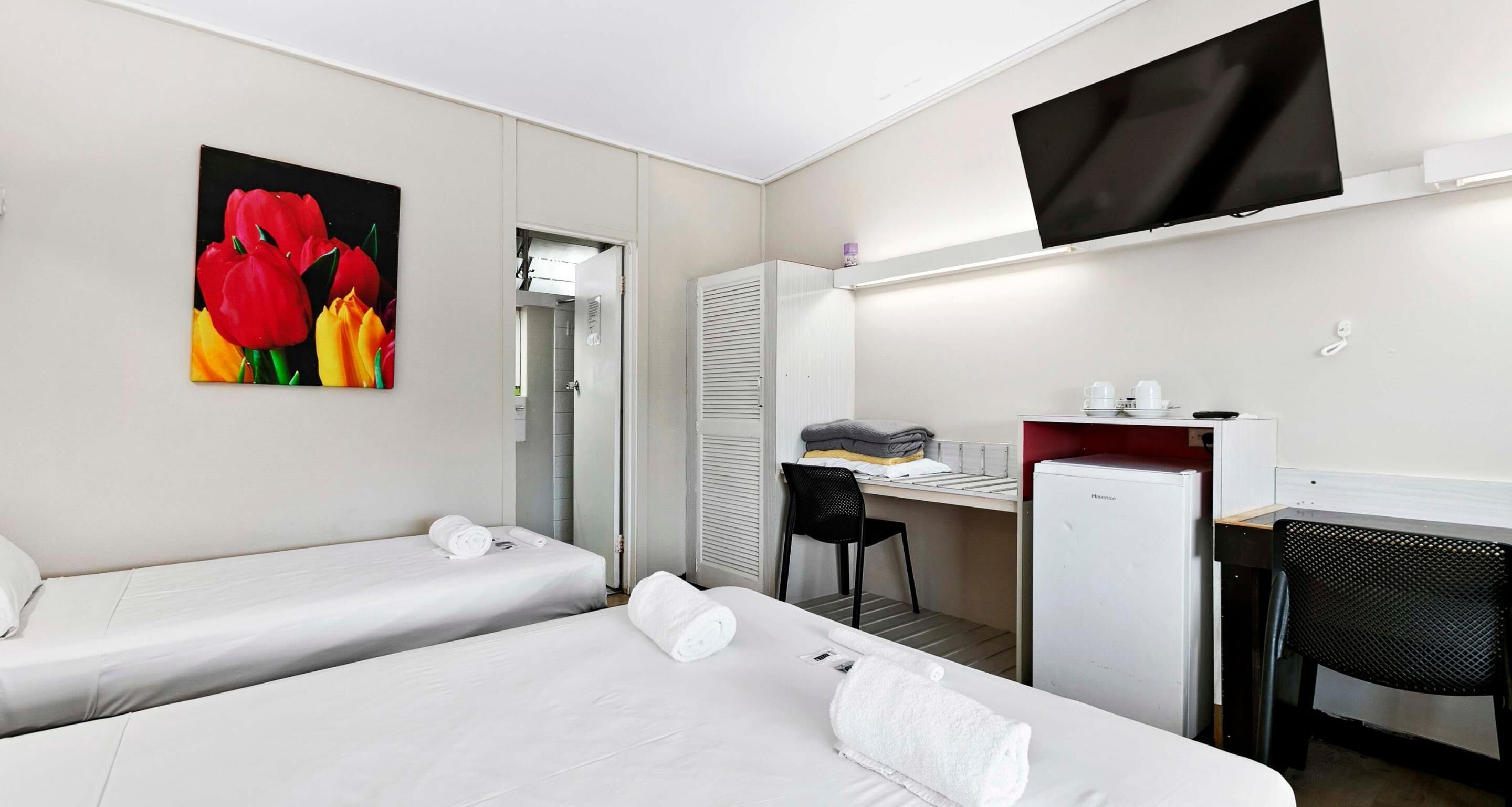 Una habitación de hotel con dos camas, un escritorio, una silla, un televisor y un refrigerador.