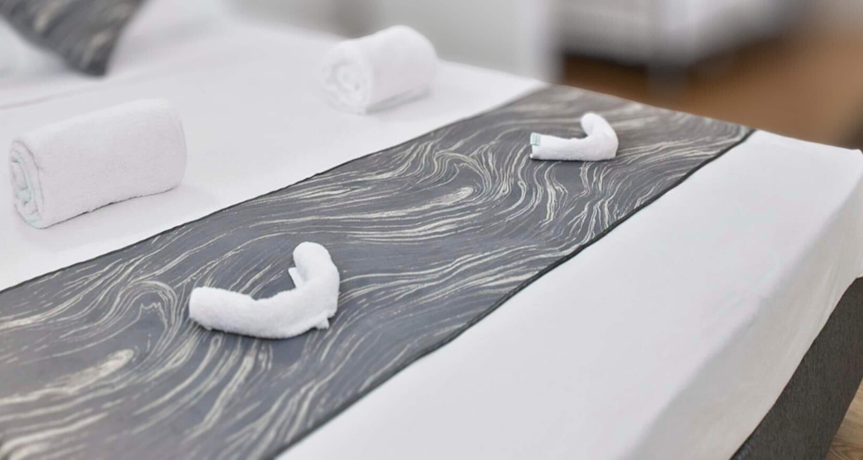 A neatly made bed with white linens and a grey patterned headboard.
