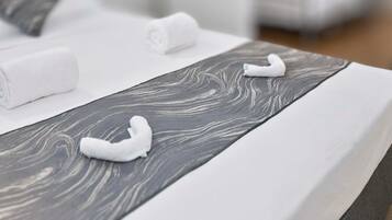 A neatly made bed with white linens and a grey patterned headboard.