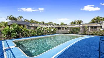 Una piscina con agua cristalina, rodeada por un deck azul y vegetación tropical.