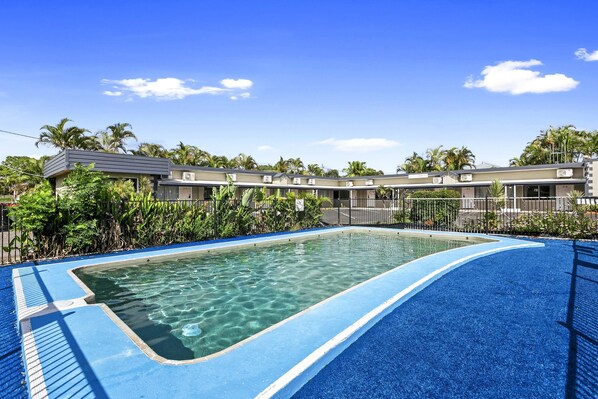 A swimming pool with clear water, surrounded by a blue deck and tropical vegetation.