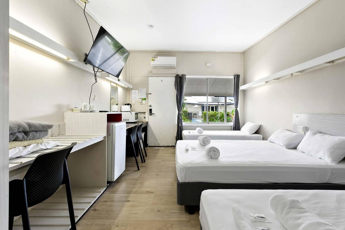Hotellihuone, jossa on kaksi sänkyä, työpöytä, tuoli, televisio ja ikkuna, josta on näkymä vehreään maisemaan.