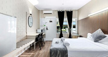Habitación de hotel con cama, escritorio, silla, microondas, ventana con cortinas y vista al exterior.