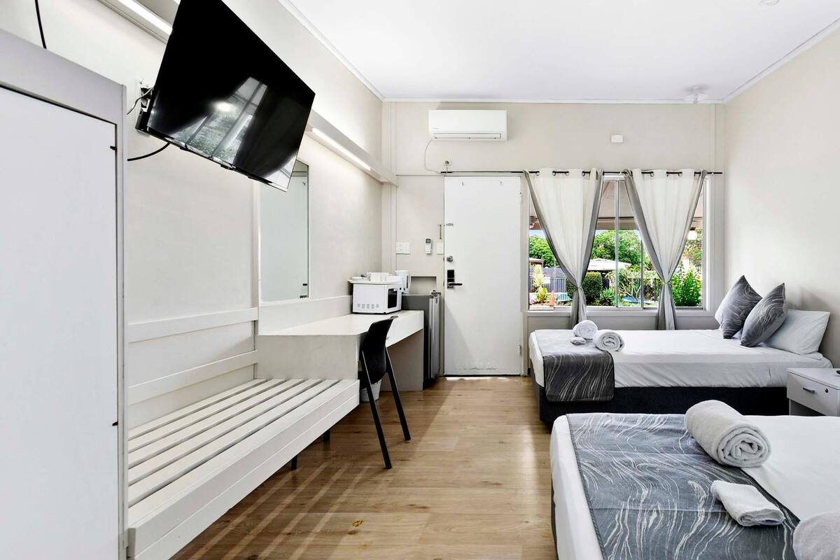 Moderni hotellihuone, jossa on työpöytä, kaksi sänkyä, televisio ja ikkuna, jossa on verhot.