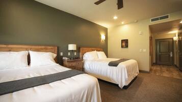 A hotel room with two beds, a ceiling fan, a nightstand with a lamp, and a door leading to another room.