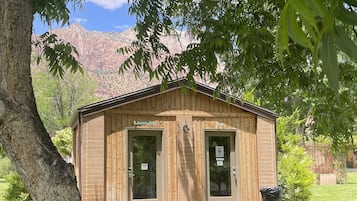 A small wooden building with two doors, one labeled "Laundry," and a tree in the foreground.