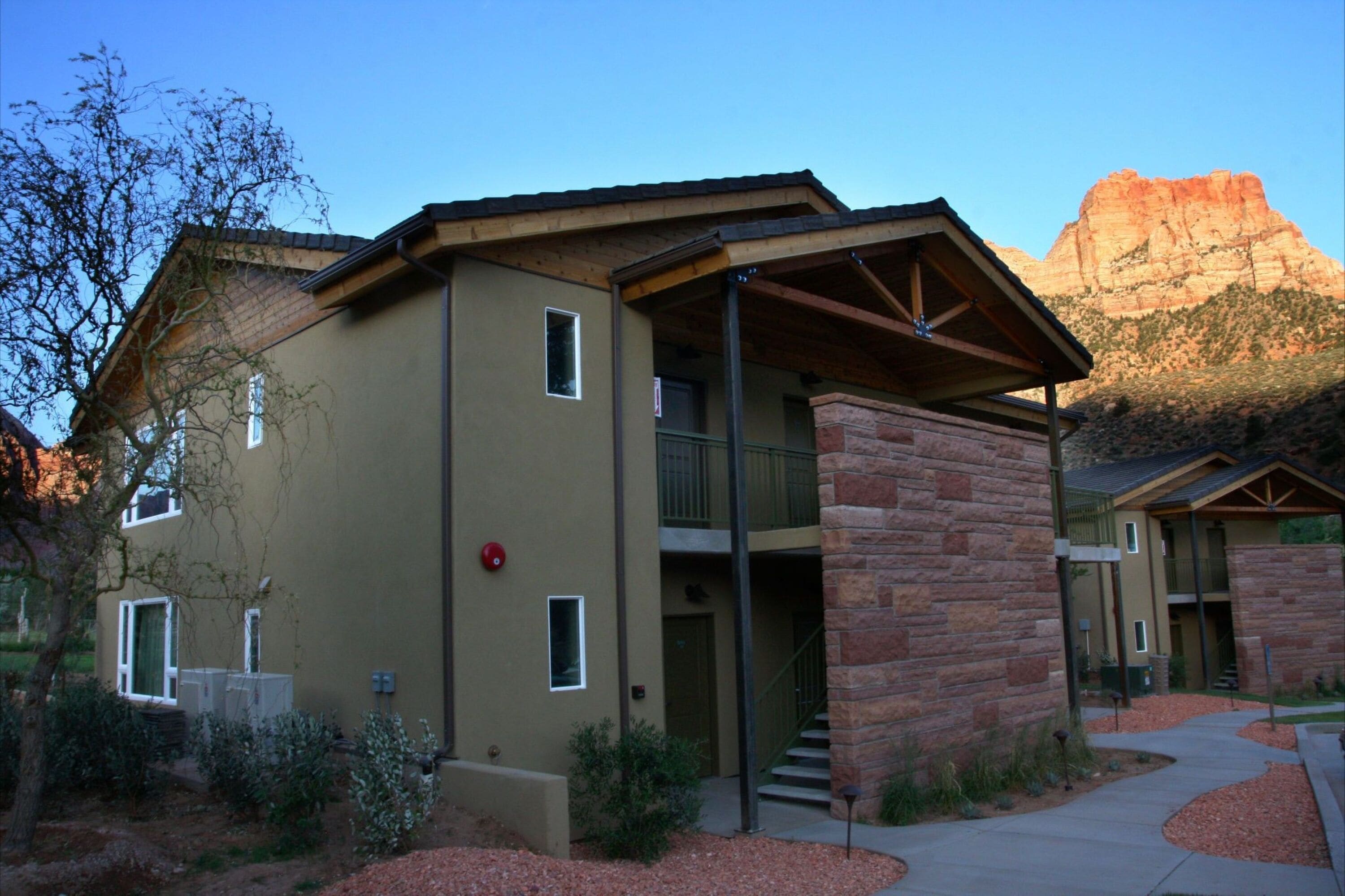 A multi-story building with a stone facade, a covered entrance, and a view of a mountain in the background.