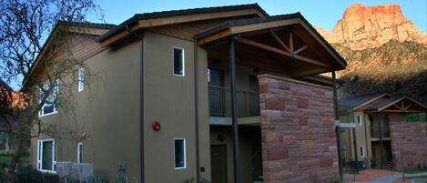 A multi-story building with a stone facade, a covered entrance, and a view of a mountain in the background.