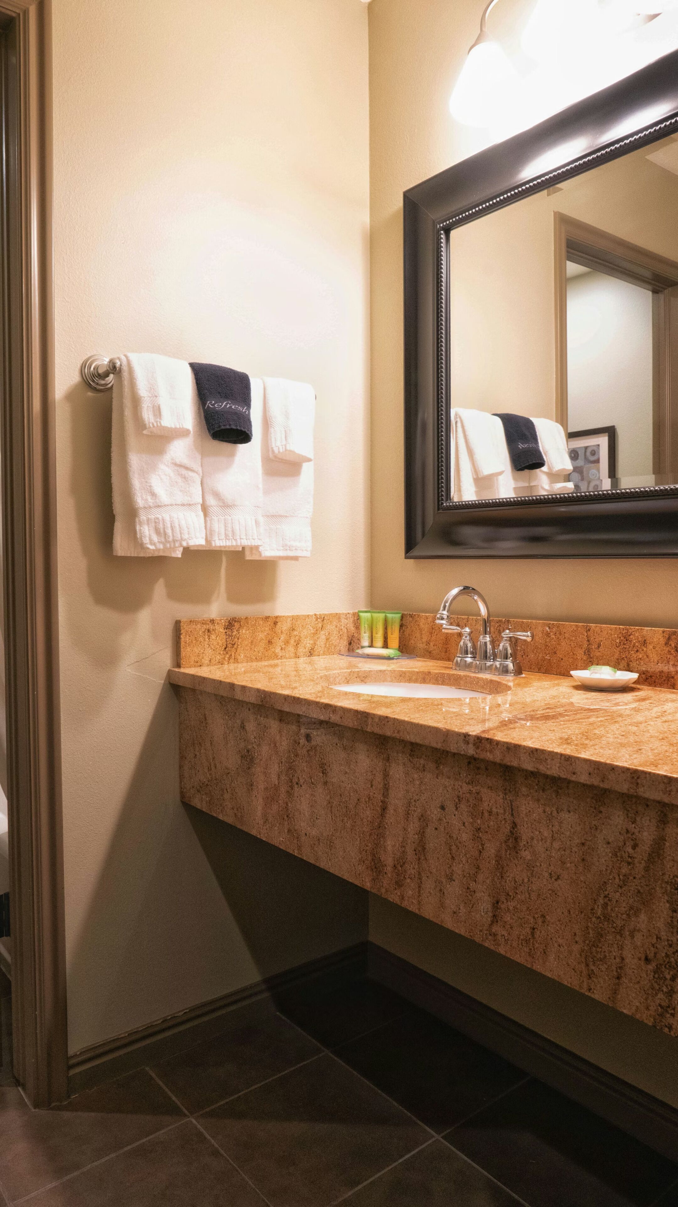 A bathroom with a granite countertop, a sink, a mirror, and two towels hanging on a towel rack.